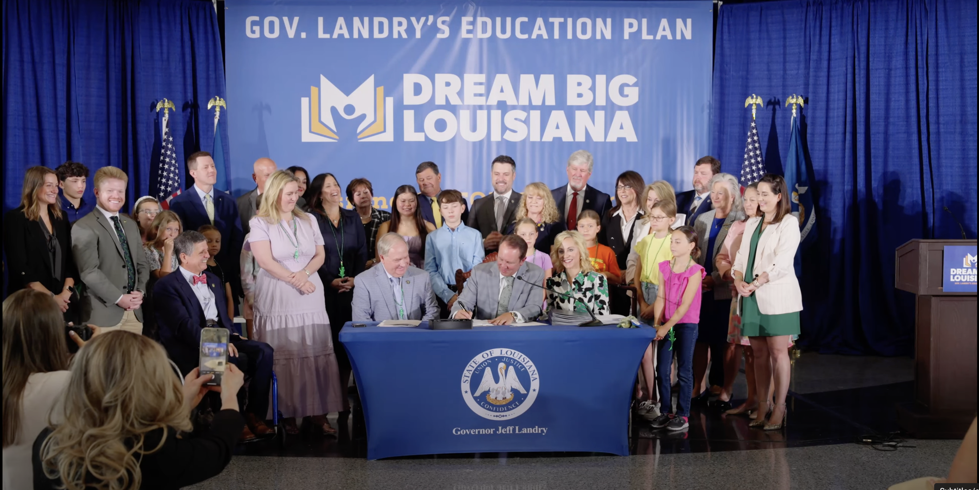 Photograph of Governor Landry signing documents with people surrounding him